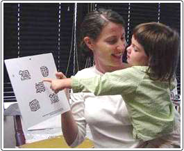 Pre-literate child choosing Wright figure during visual acuity testing. The image is on a corresponding chart held by the examiner. The child selects the image that matches the one being pointed to by the tester.